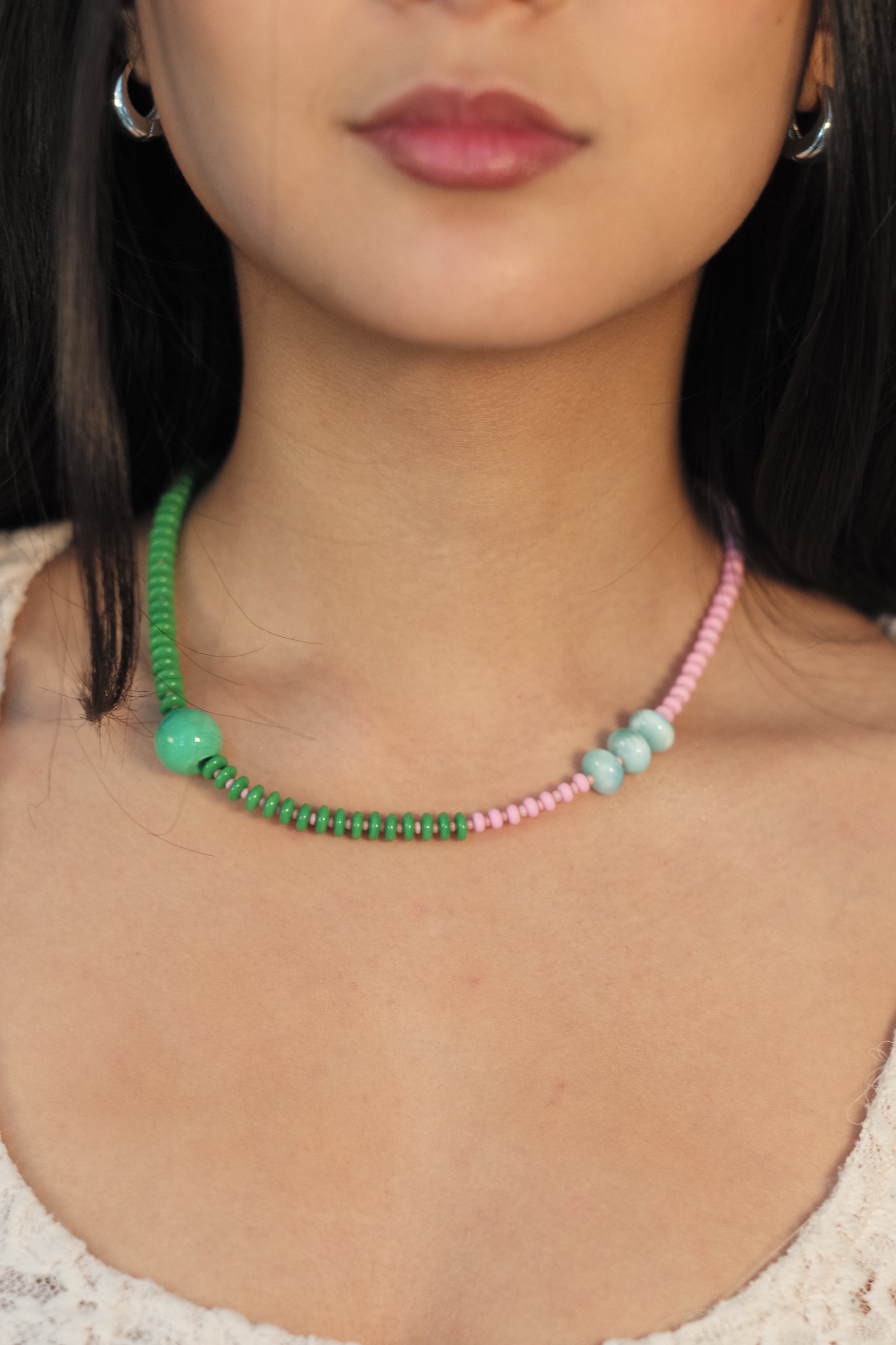 Close-up of a person wearing a green and pink beaded necklace on a textured surface.