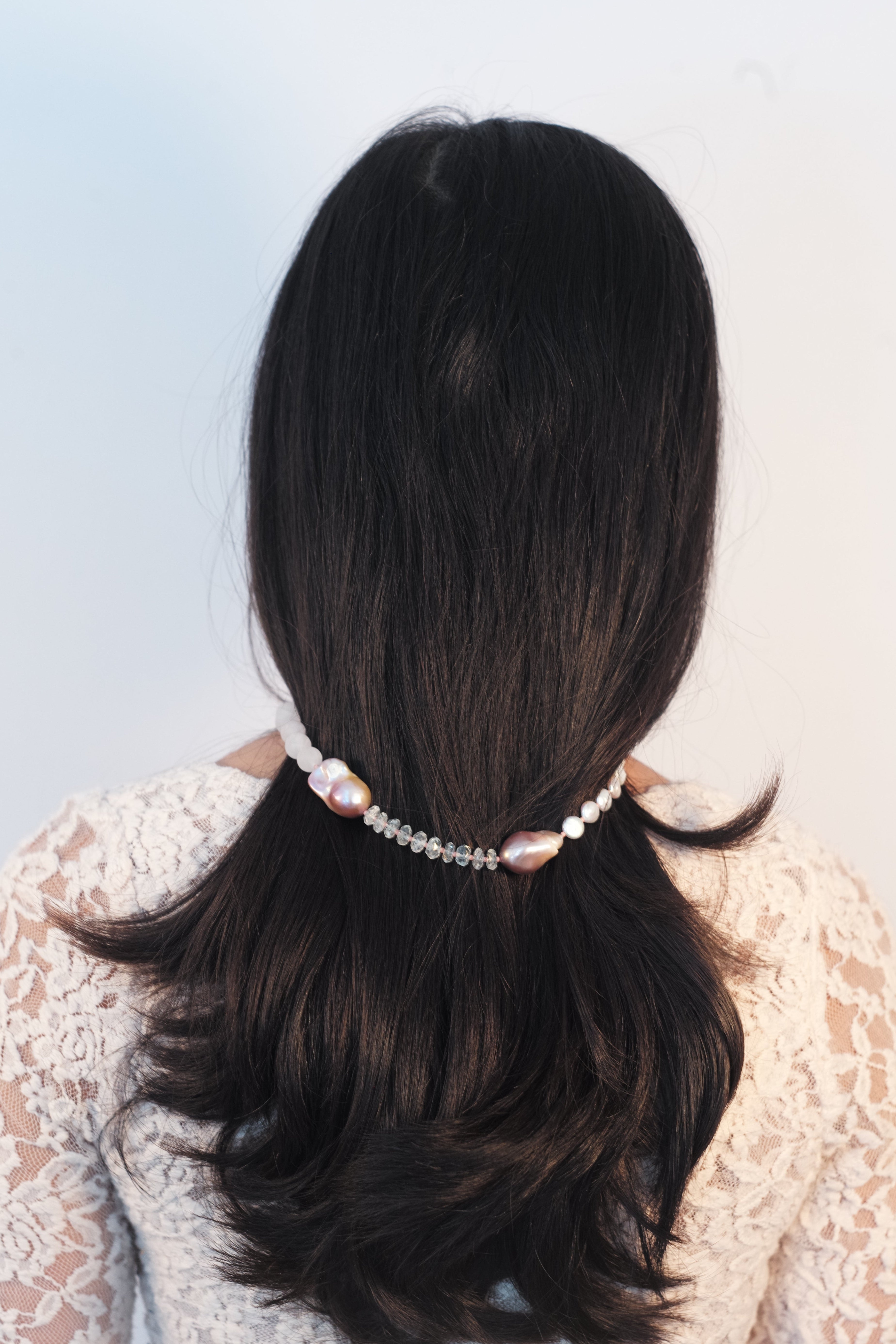 Two braided ponytails with a pearl hair tie on a light blue background