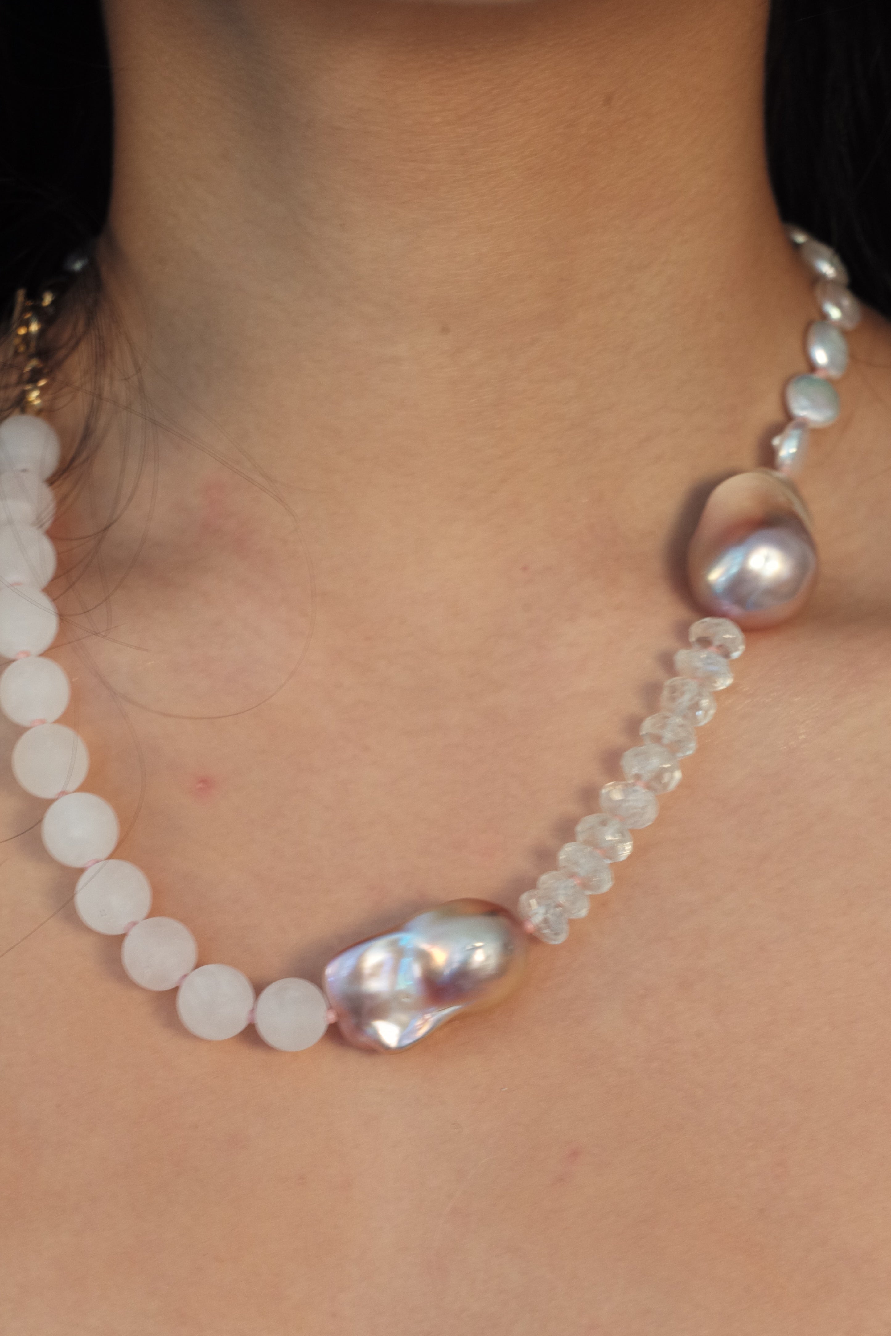 Pearl necklace being worn on a person's neck with a lace garment in the background