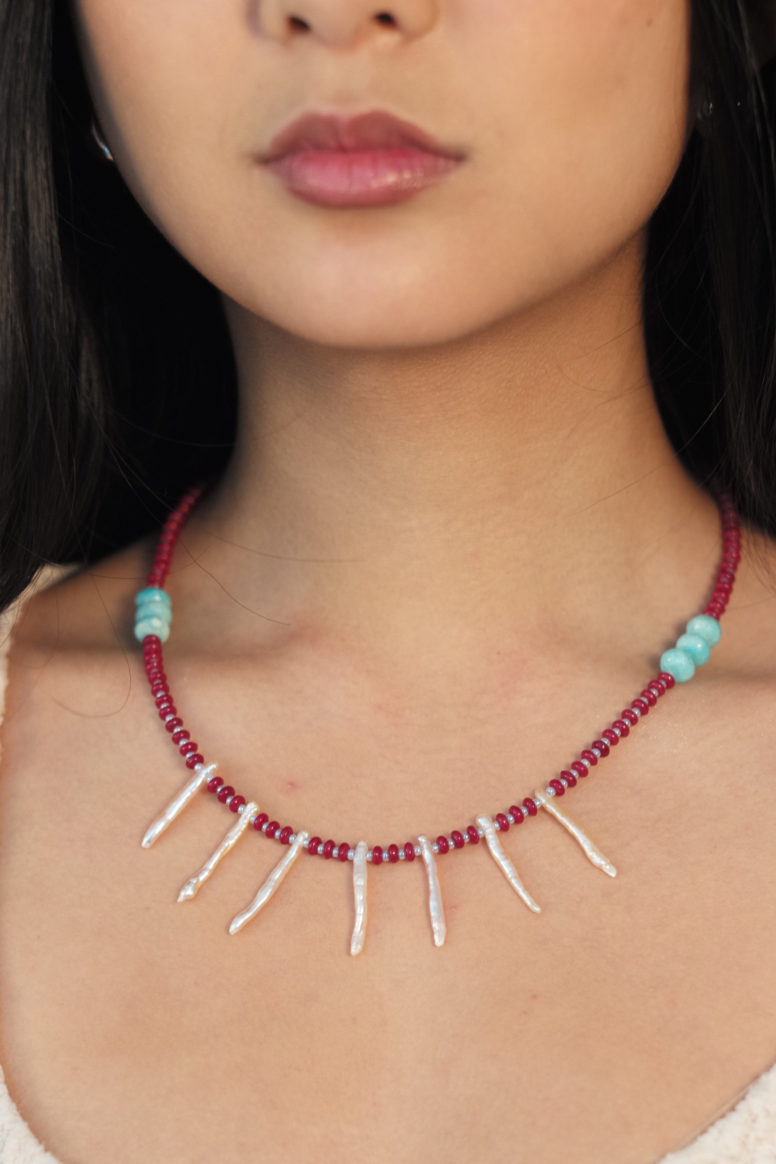 Close-up of a person wearing a red beaded necklace with turquoise stones on a textured surface.