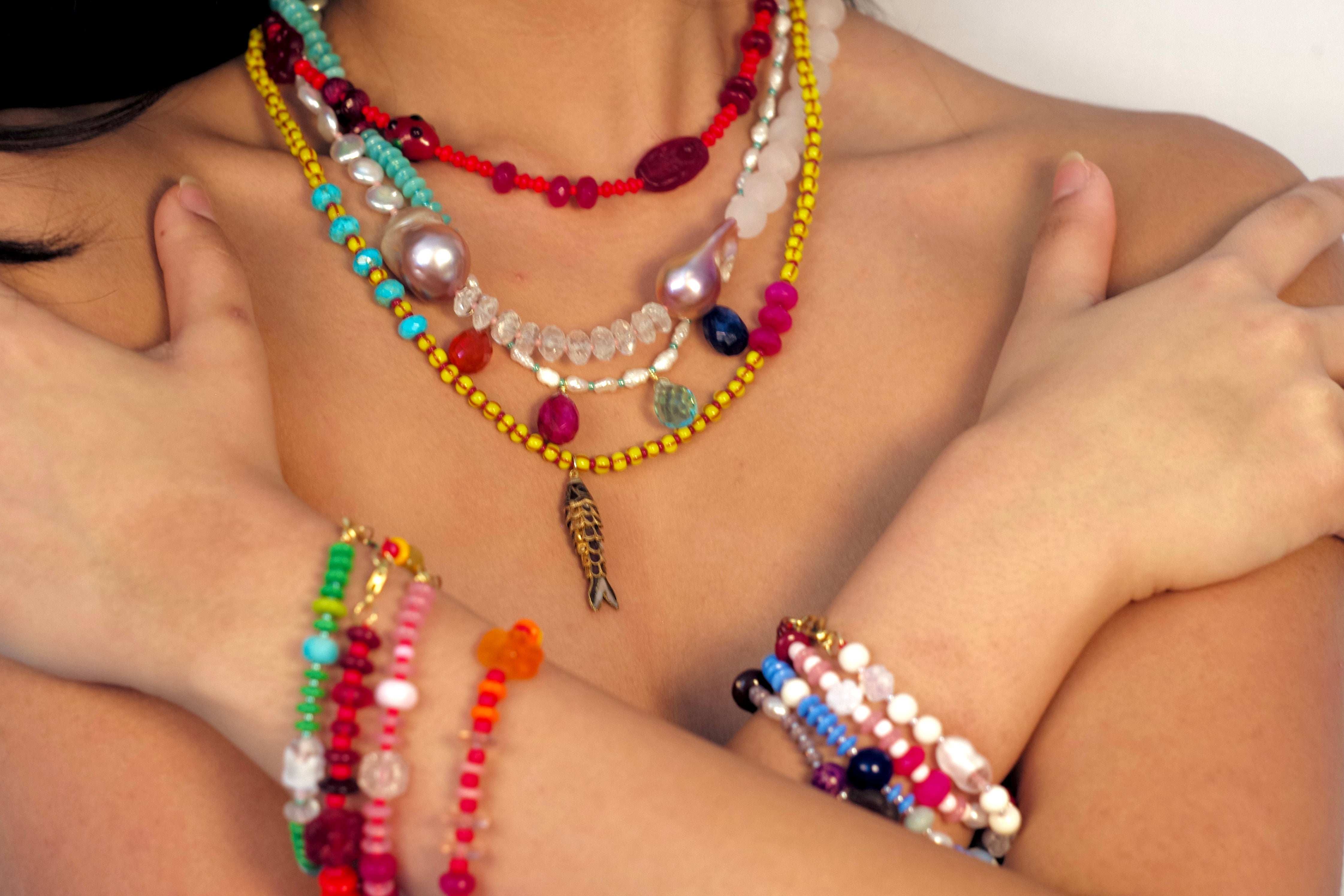 Colorful beaded necklaces and bracelets on a person against a white background
